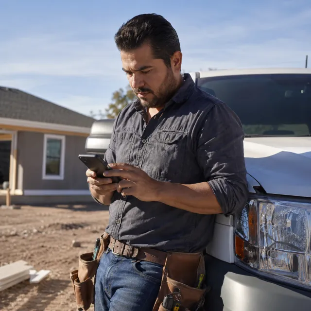 El técnico apoyado en su camioneta prepara una cotización en el teléfono